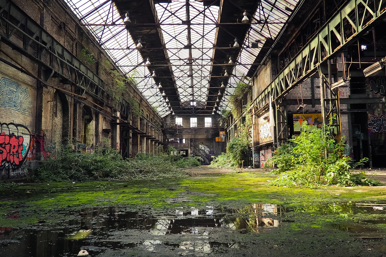 a building that has a lot of graffiti on it, by Richard Carline, abandoned steelworks, overgrown with aquatic plants, interior view, rain lit