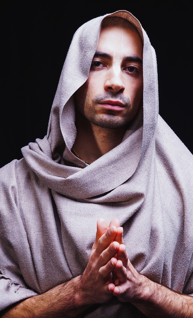 a man with his hands folded in prayer, an album cover, inspired by Taddeo Gaddi, shutterstock, draped in flowing fabric, joe rogan, hood, portrait shot 8 k