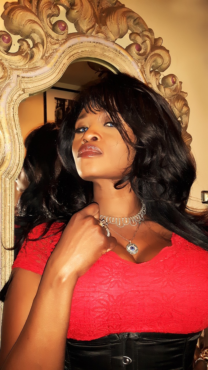 a woman in a red dress posing in front of a mirror, inspired by Chinwe Chukwuogo-Roy, happening, with full bangs, seductive look, diamonds around her neck, closeup photo