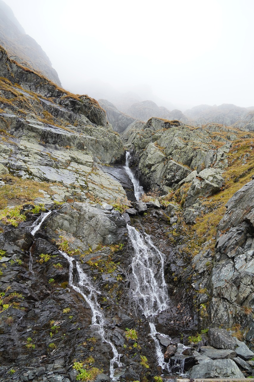 a waterfall flowing down the side of a mountain, by Werner Andermatt, autumn rain turkel, very known photo, in low fog, wide shot photo