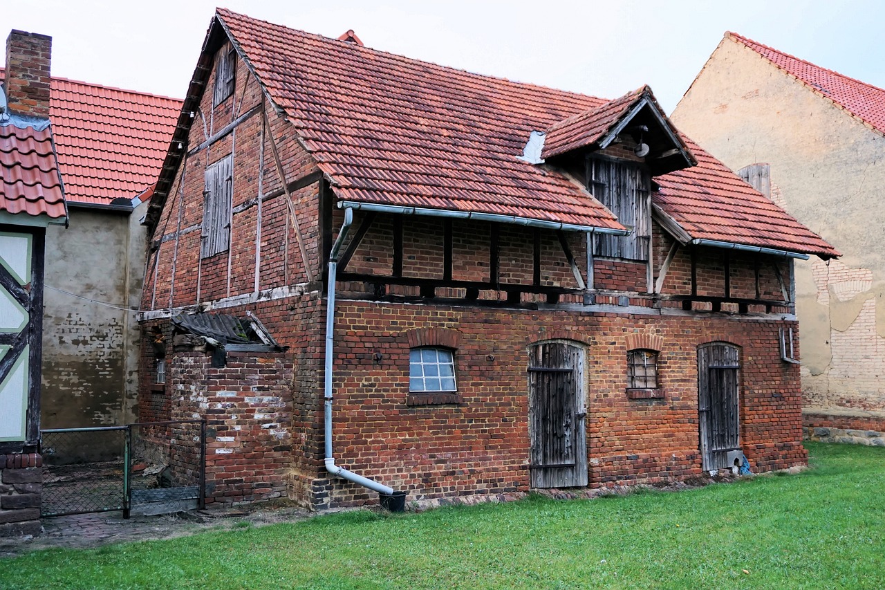 a brick house sitting on top of a lush green field, by Karl Hagedorn, pixabay, renaissance, a ghetto in germany, of augean stables, warehouse, front side view