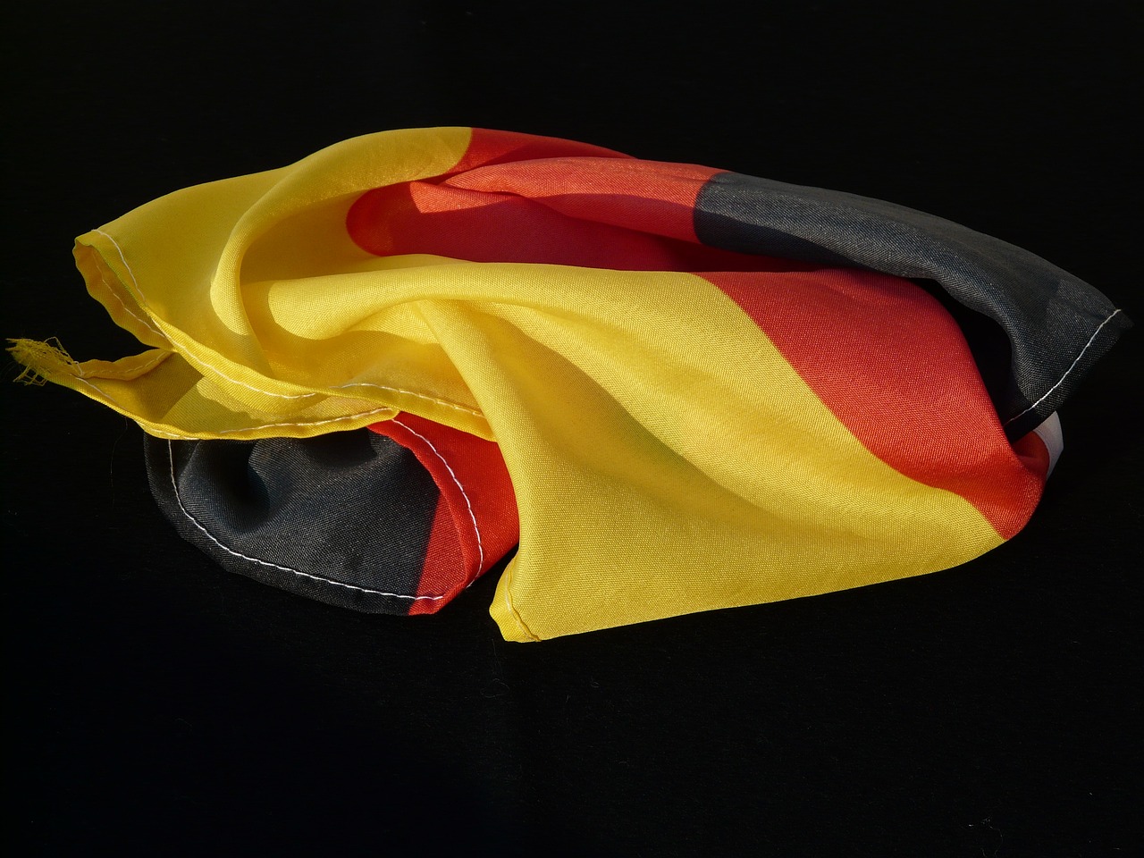 a red, yellow and black flag laying on top of a black surface, bauhaus, head scarf, germany, chiffon, folded