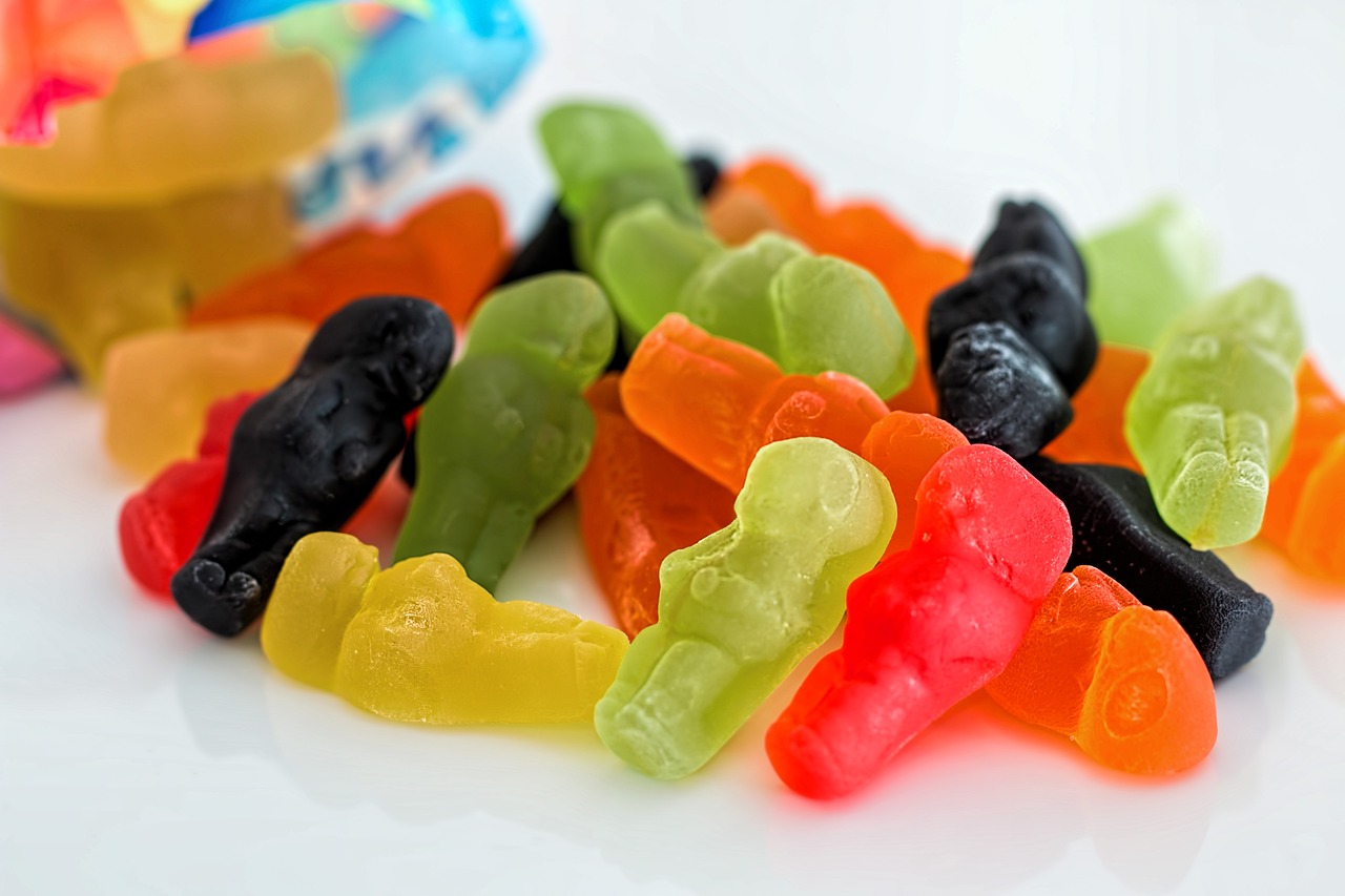 a pile of gummy bears sitting on top of a table, a stock photo, inspired by Władysław Podkowiński, sexy, jackstraws, with a figure in the background, close-up product photo