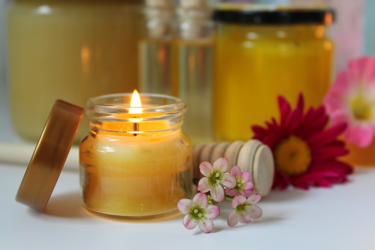 a candle sitting on top of a table next to flowers, by Rhea Carmi, pexels, jar of honey, light from bottom, close-up product photo, full res