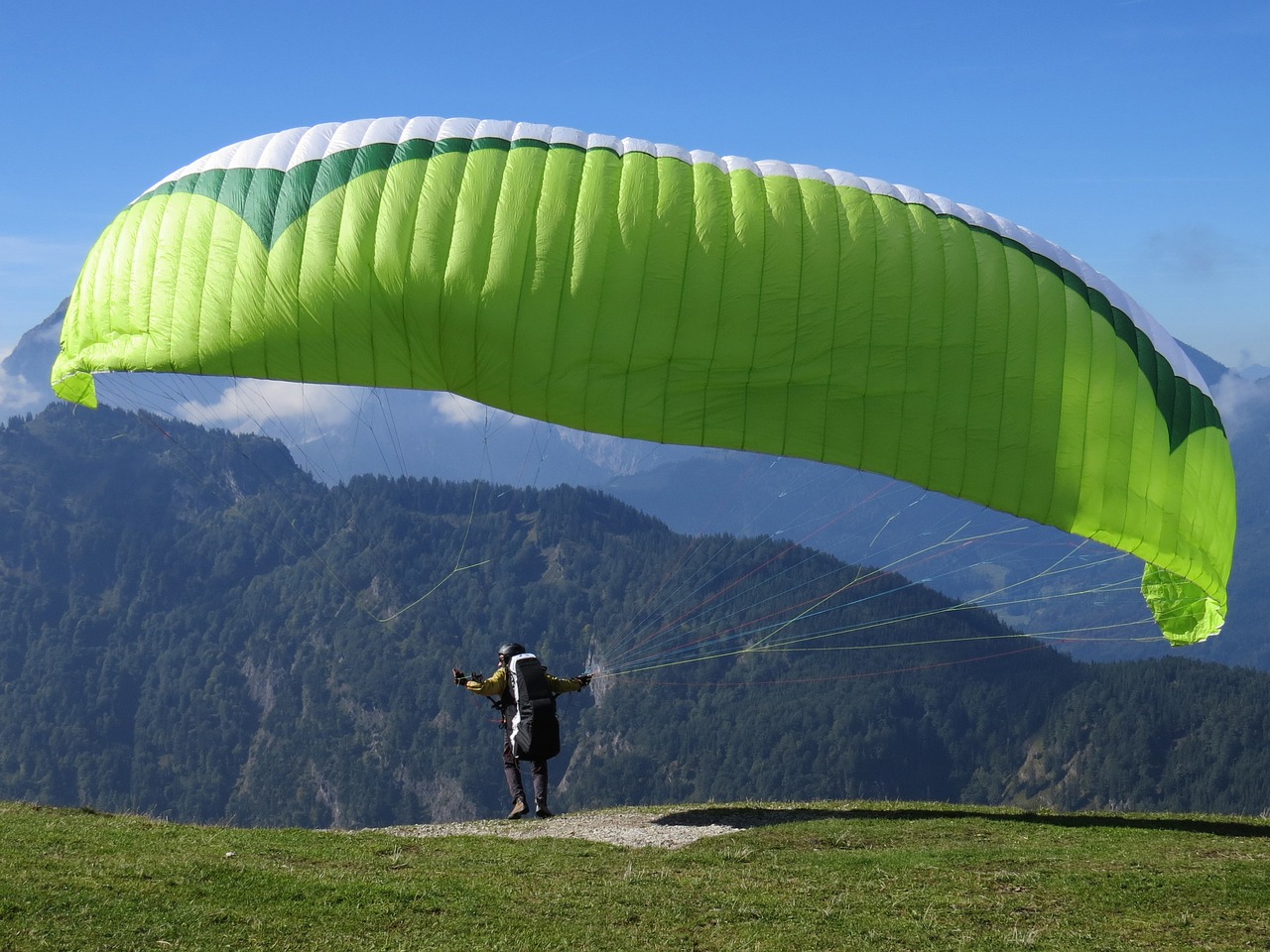 a man standing on top of a lush green hillside, a picture, by Werner Andermatt, parachutes, 8 k. filling of the view, wing, flash photo