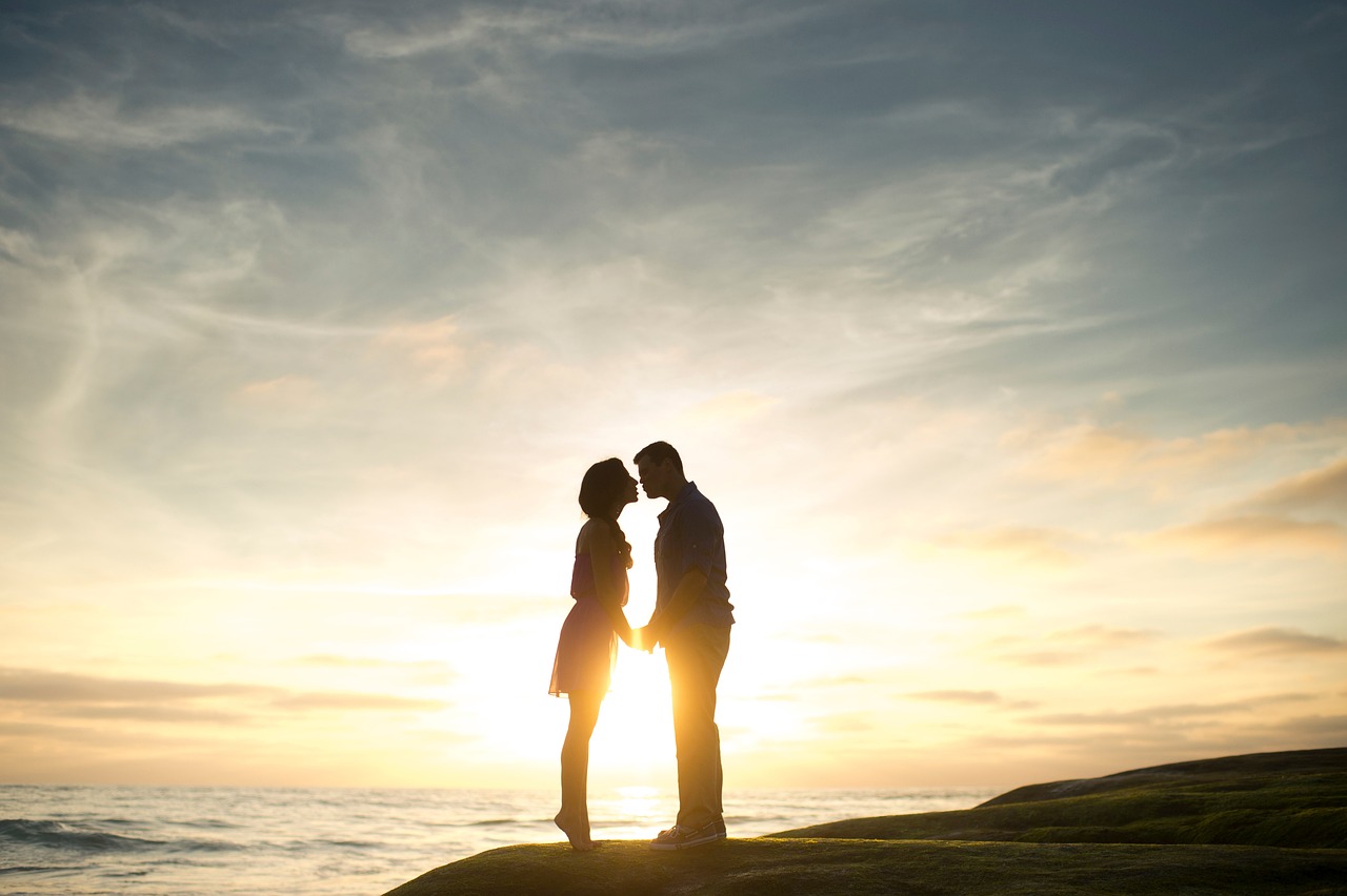 a couple standing on top of a rock next to the ocean, romanticism, backlit, istockphoto, facing each other, compassionate