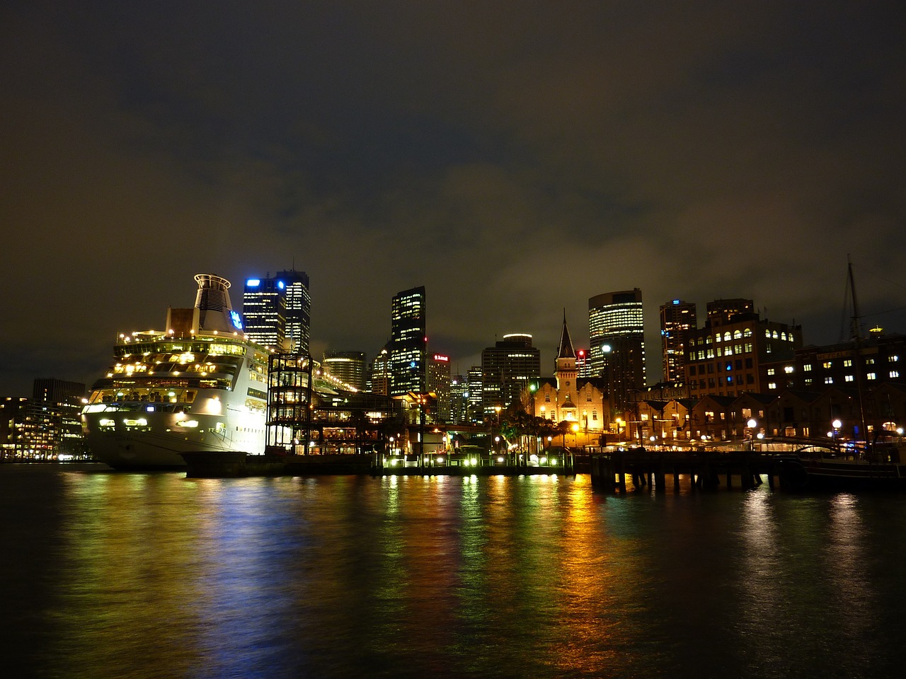 a large body of water with a city in the background, a photo, by Jay Hambidge, flickr, hurufiyya, victorian harbour night, beautifully lit buildings, viewed from the harbor, vibrant but dreary