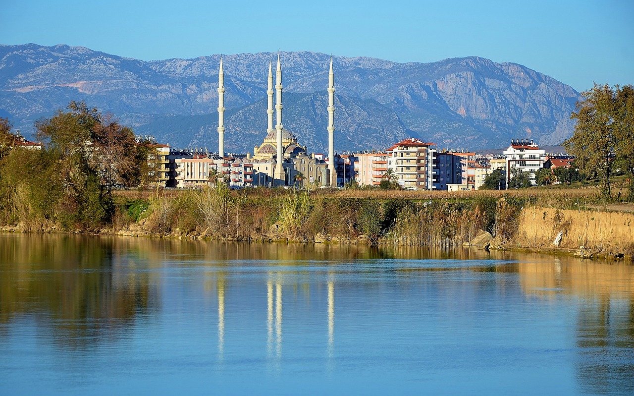 a body of water with buildings and mountains in the background, by Ibrahim Kodra, shutterstock, hurufiyya, tall spires, turkey, tarski fiume, blue reflections