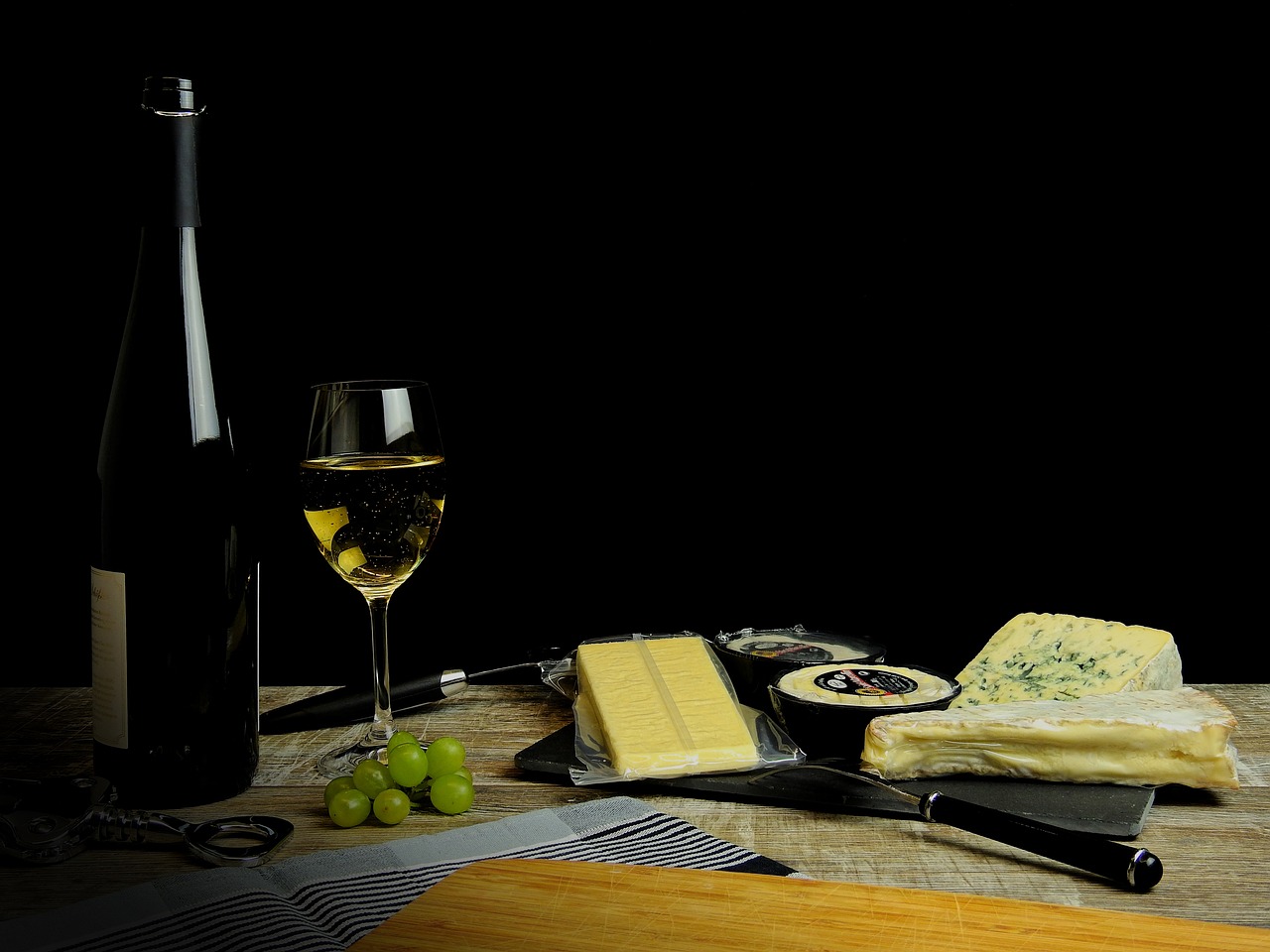 a bottle of wine, cheese and grapes on a table, a still life, by Thomas Häfner, pexels, on a black background, butter, miniature product photo, close-up product photo