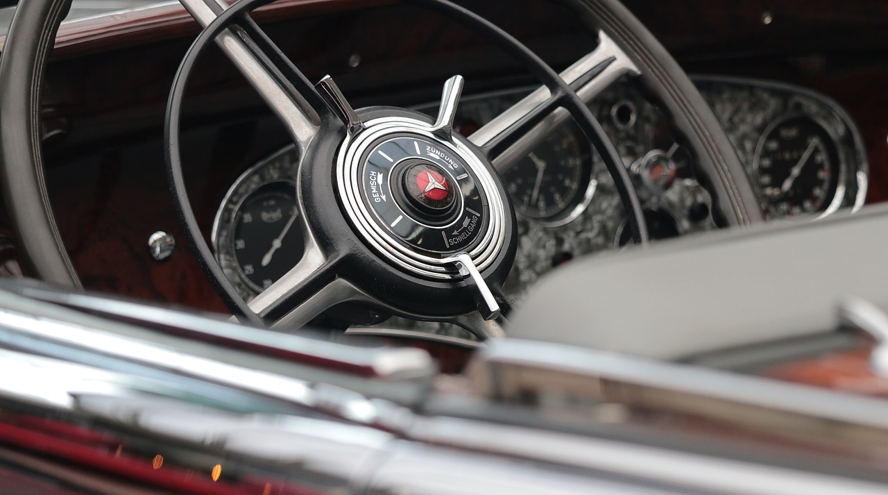a close up of a steering wheel in a car, by Jay Hambidge, retrofuturism, classic cars, wine-red and grey trim, bokeh chrome accents, [ [ hyperrealistic ] ]