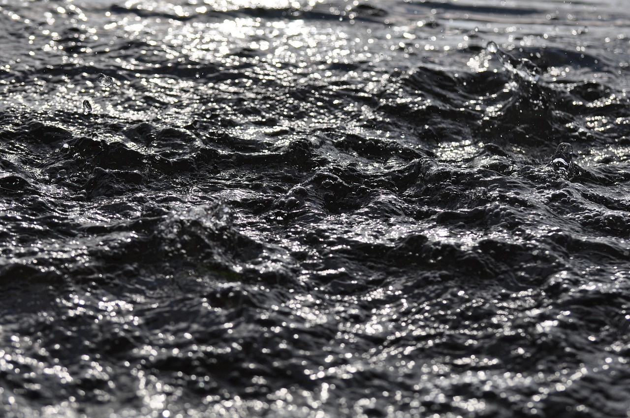 a close up of a body of water, hurufiyya, covered with liquid tar. dslr, rain lit, waves, sunlight reflected on the river