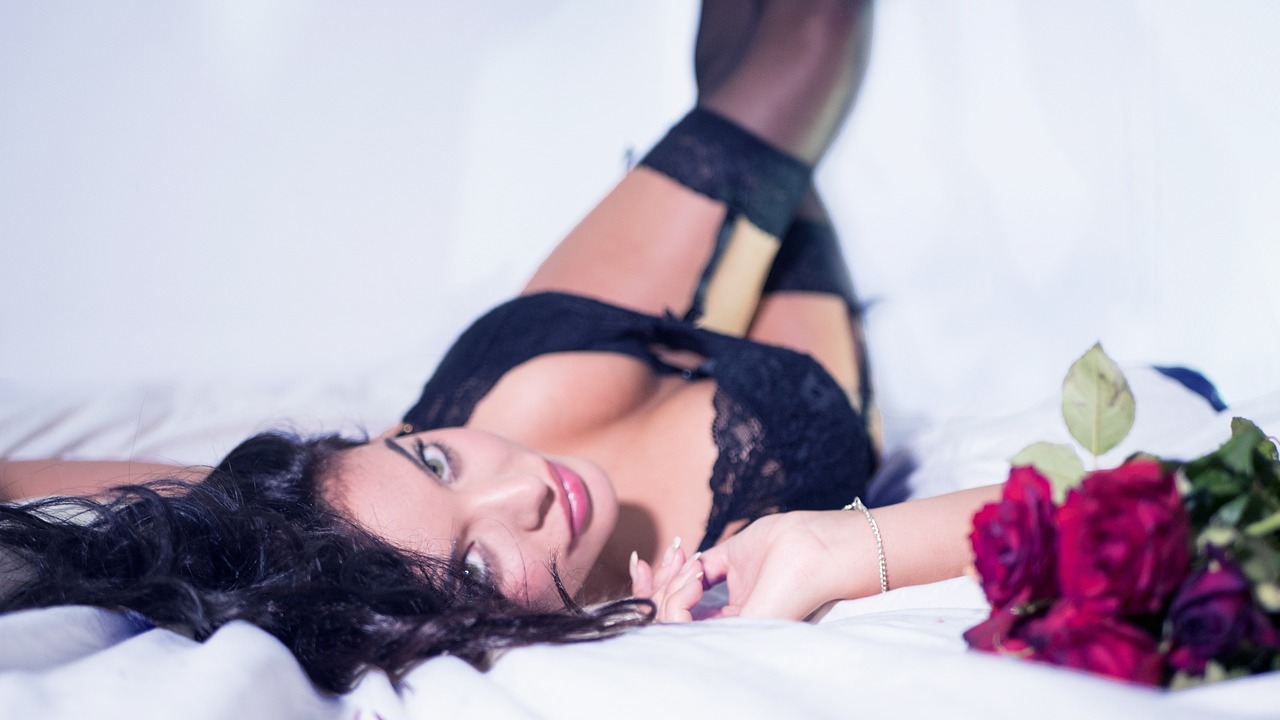 a woman laying on top of a bed next to a bouquet of flowers, a photo, by Matt Cavotta, arabesque, very sexy woman with black hair, wearing in stocking, high angle close up shot, avatar image
