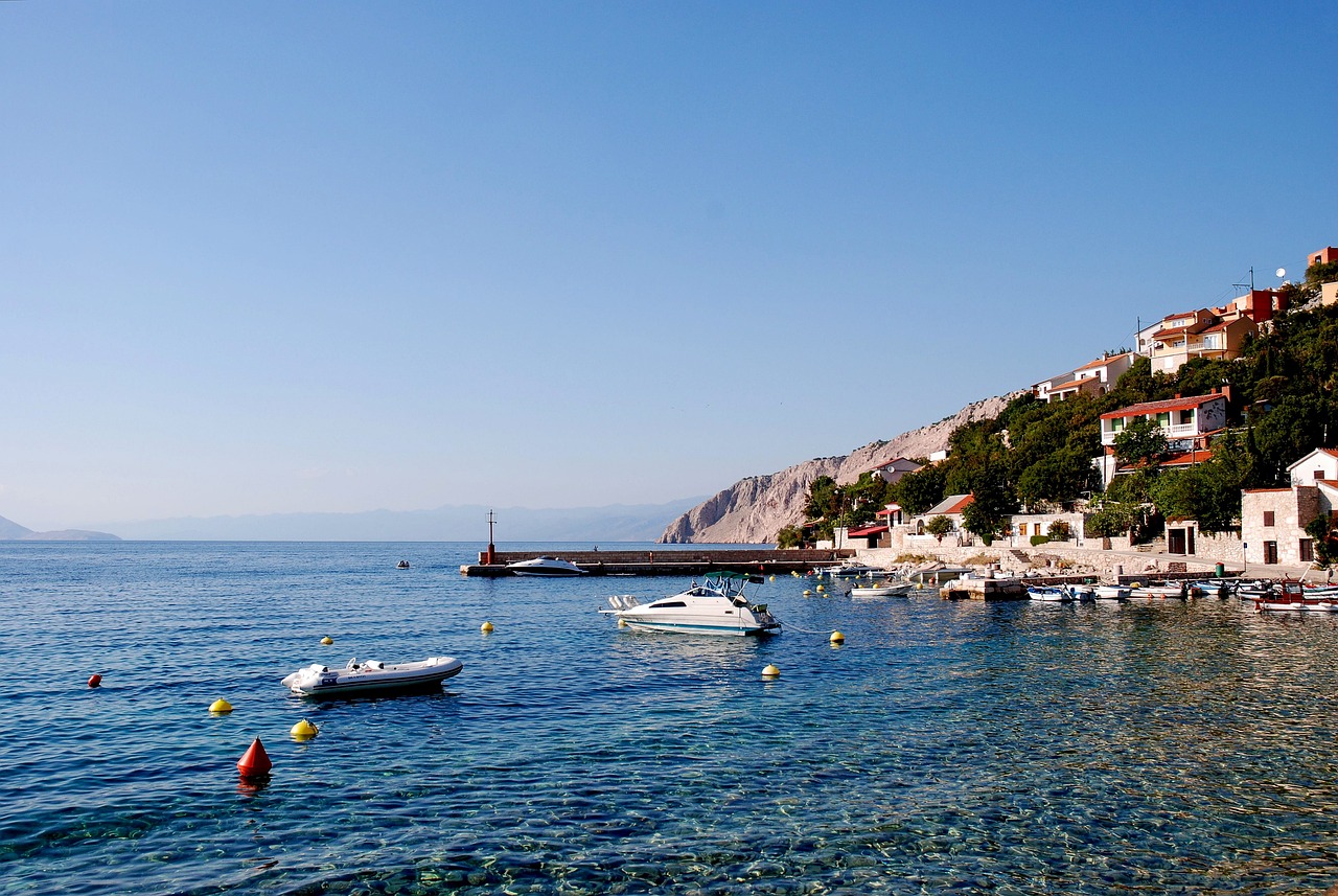 a group of boats floating on top of a body of water, a picture, by January Suchodolski, mediterranean beach background, small port village, clear blue skies, benjamin vnuk