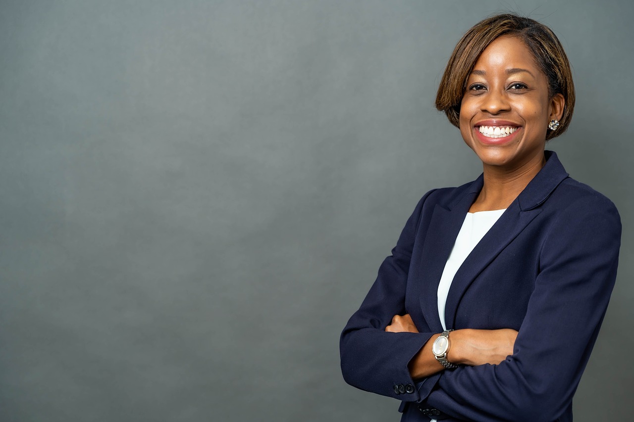 a woman in a business suit standing with her arms crossed, a portrait, by Malvin Gray Johnson, pexels, radiant smile. ultra wide shot, portrait photo of a backdrop, on a gray background, having a great time