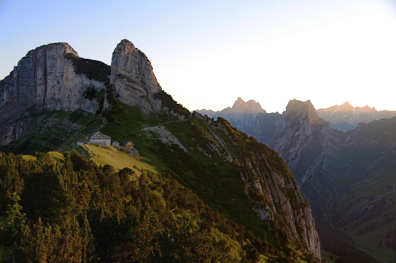 a group of sheep standing on top of a lush green hillside, a picture, by Hans Werner Schmidt, les nabis, sun rises between two mountains, alpine architecture, 1 8 mm wide shot, cliff side at dusk