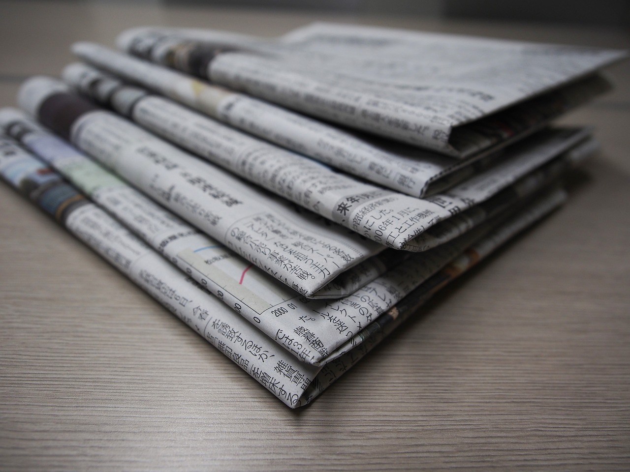 a stack of newspapers sitting on top of a wooden table, a picture, pexels, on a gray background, lined up horizontally, video, close up photo