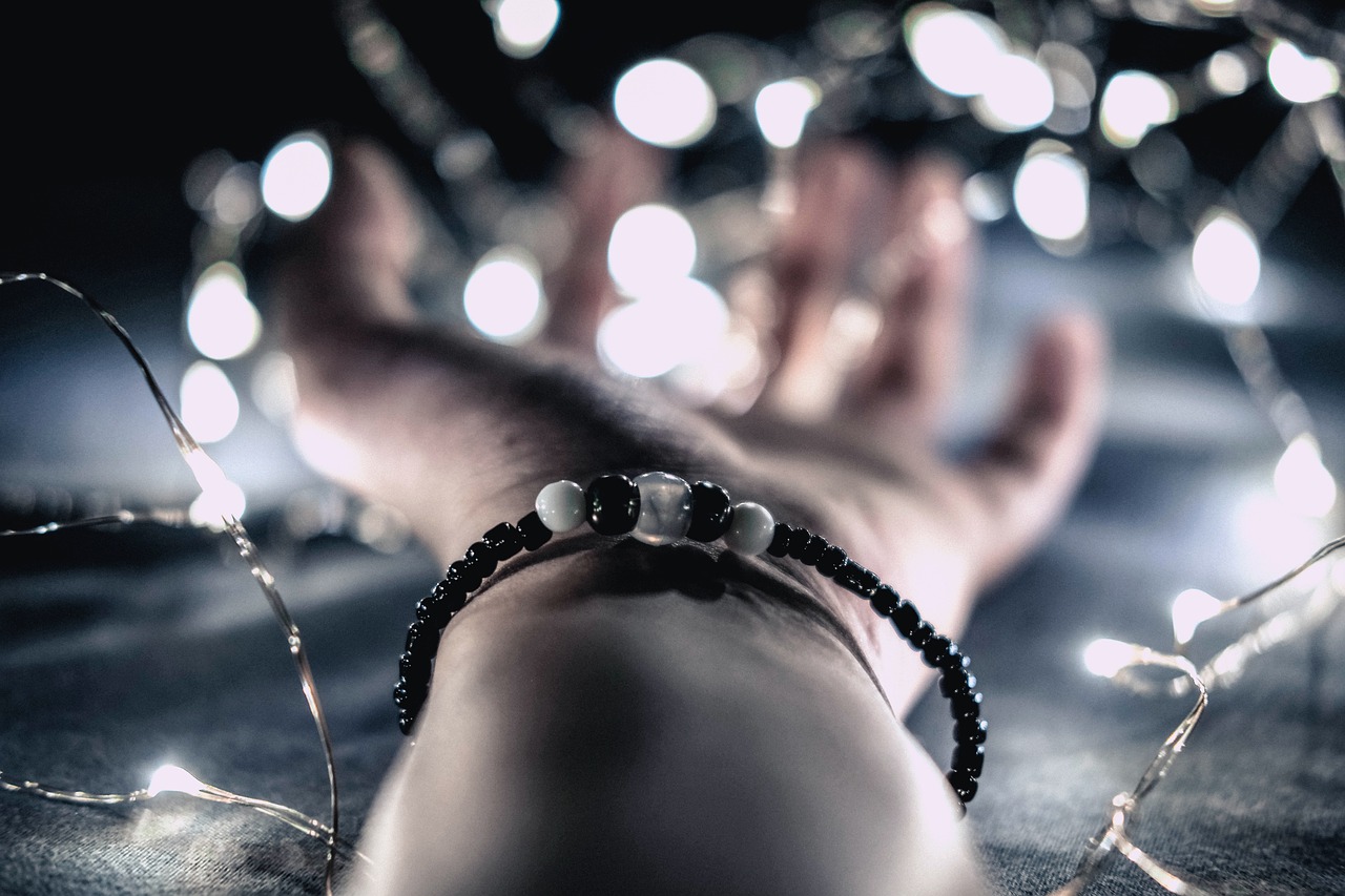 a close up of a person's hand with a string of lights in the background, by Emma Andijewska, romanticism, onyx bracelets, beads, dark and white, feet and hands