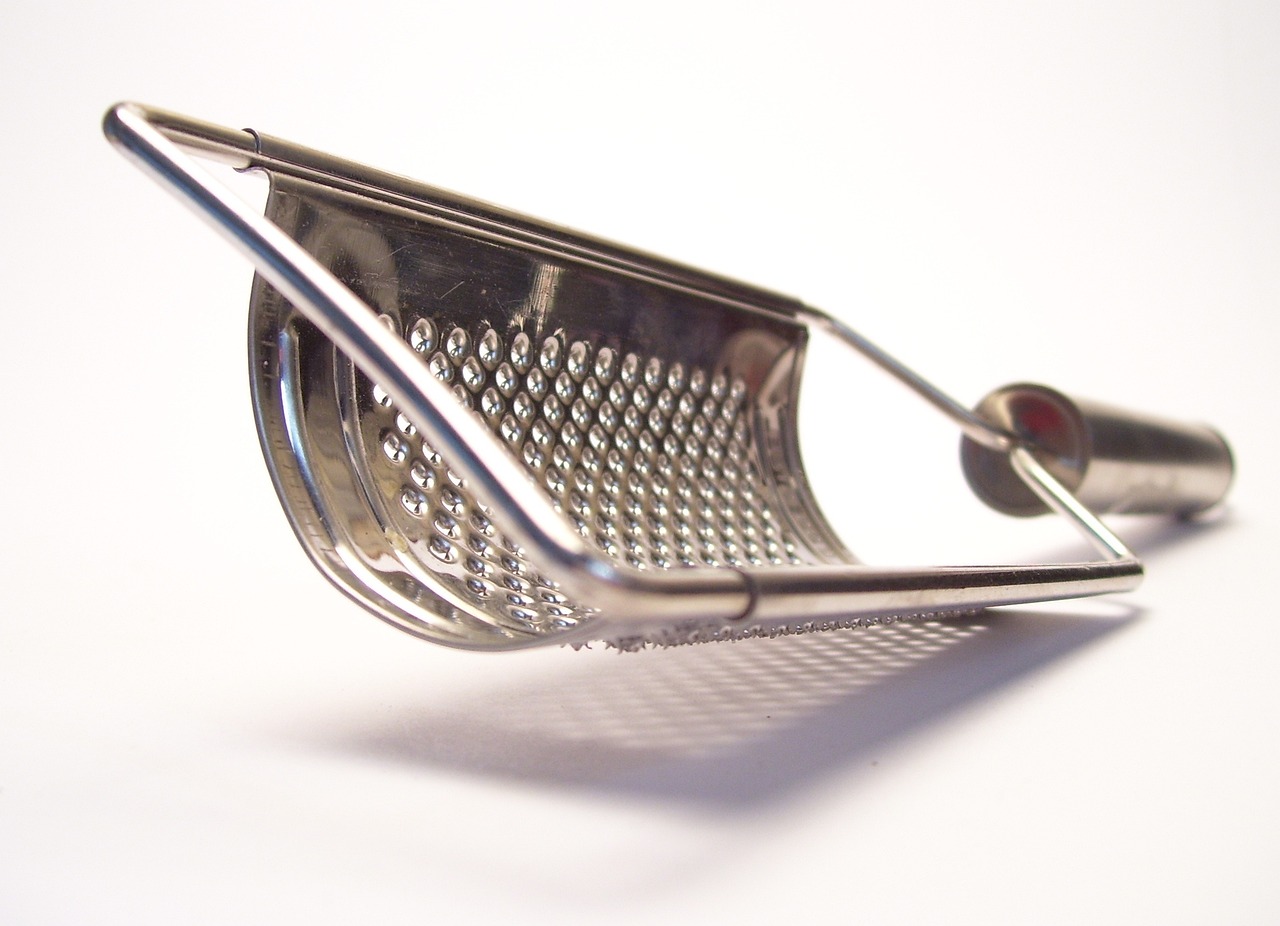 a close up of a metal grater on a white surface, by Matt Stewart, pexels, speculum, fork, viewed from the side, metal lid