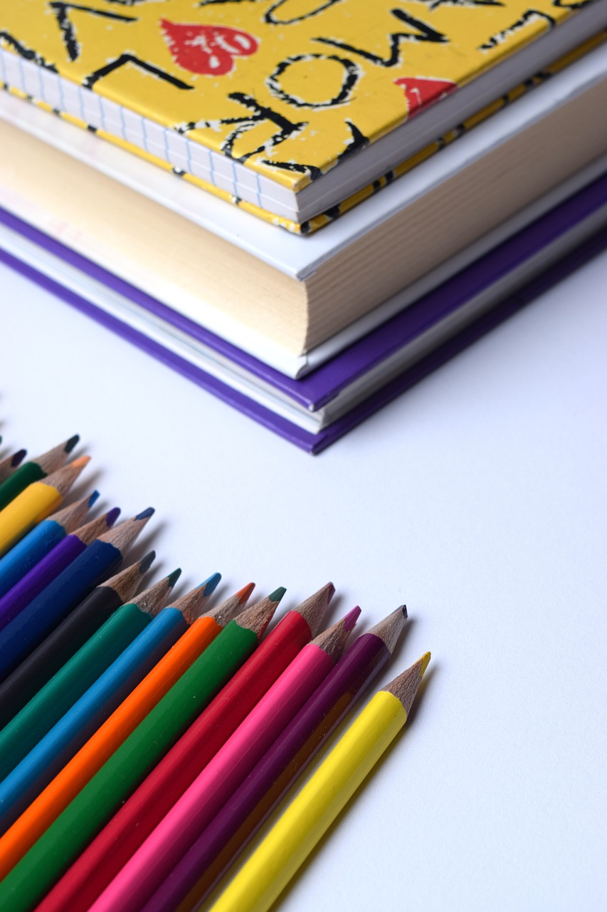 a pile of colored pencils next to a stack of books, a color pencil sketch, pexels, crayon art, purple and yellow, on white paper, seen from below, product introduction photo