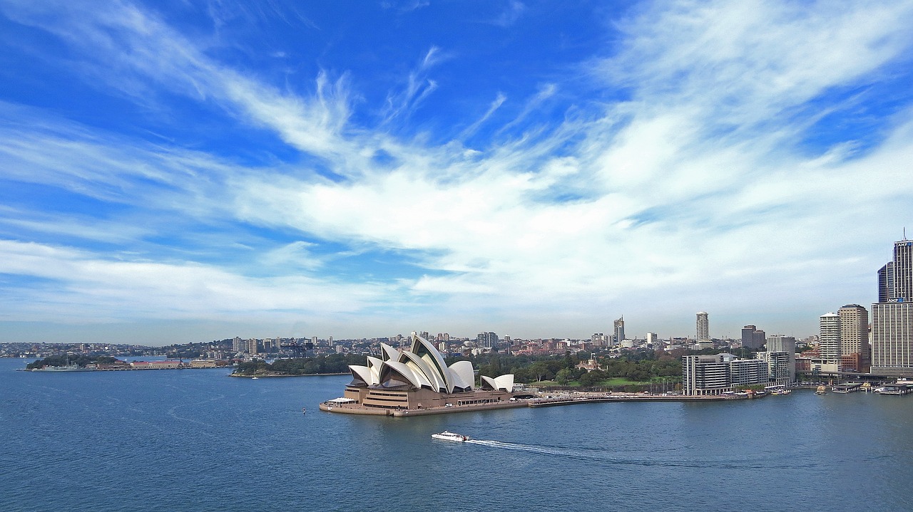 a large body of water with a boat in it, inspired by Sydney Carline, pexels, hurufiyya, blue sky with clouds, central station in sydney, sweeping vista, harmony of swirly clouds