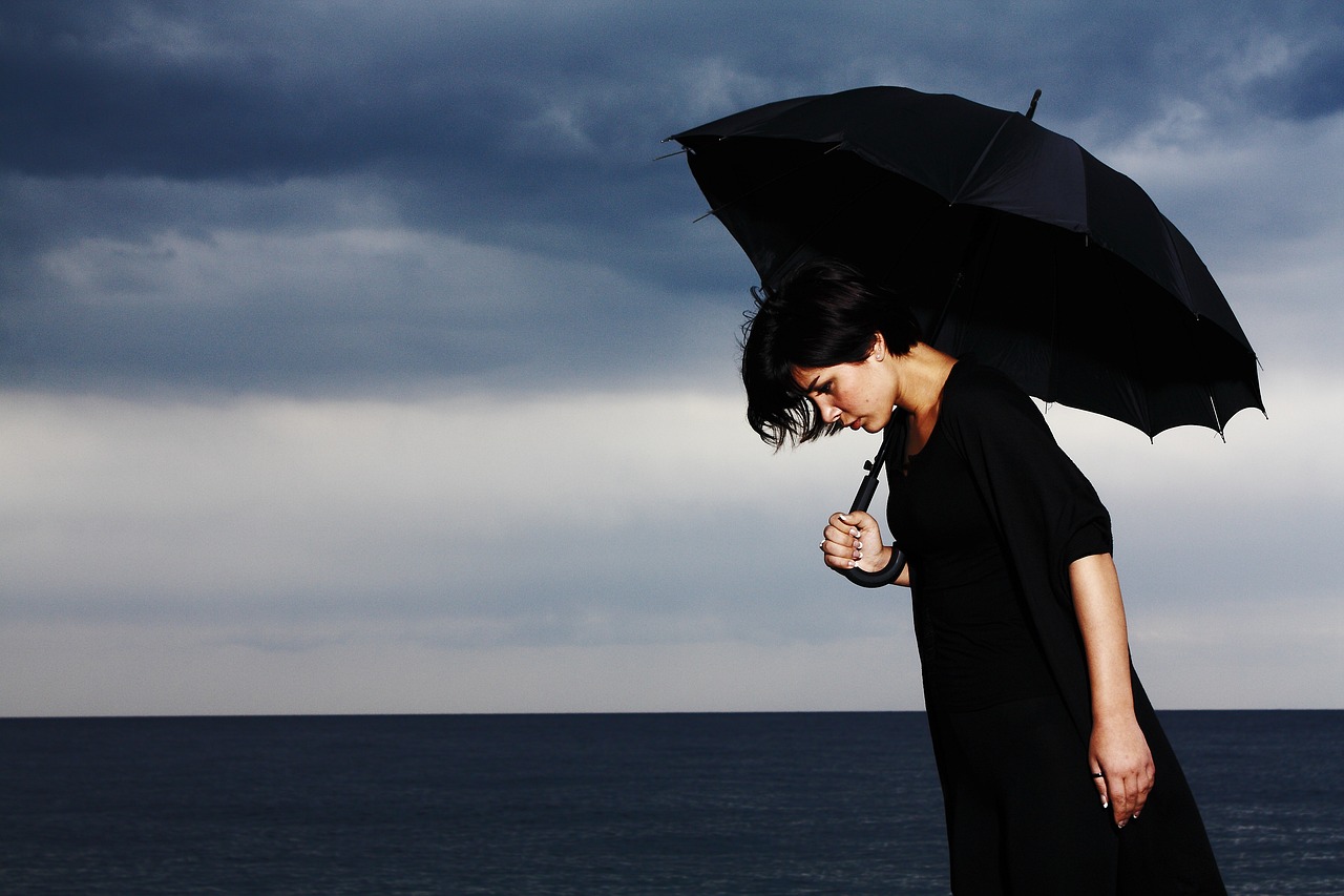 a woman in a black dress holding an umbrella, a picture, pexels, romanticism, loss in despair, style mix of æon flux, an ocean, she's sad
