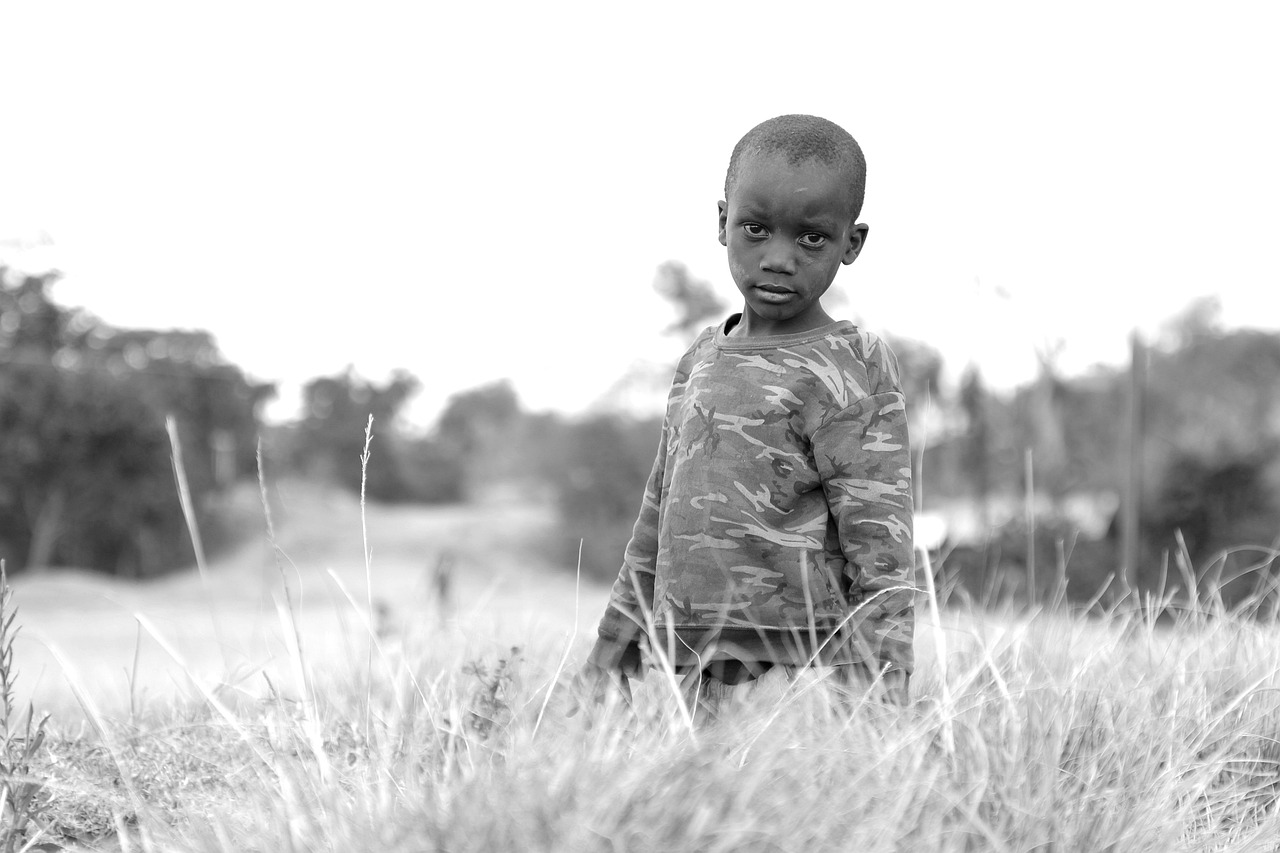 a young boy standing in a field of tall grass, a black and white photo, by Dean Ellis, flickr, hurufiyya, very kenyan, with a sad expression, standing on the field of battle, 2 years old