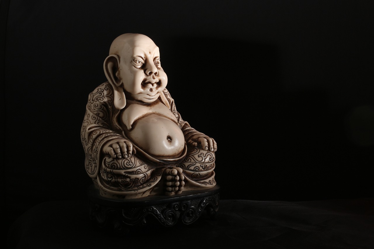 a statue of a smiling buddha sitting on a table, a statue, featured on zbrush central, cloisonnism, on black background, carved ivory, fully body photo