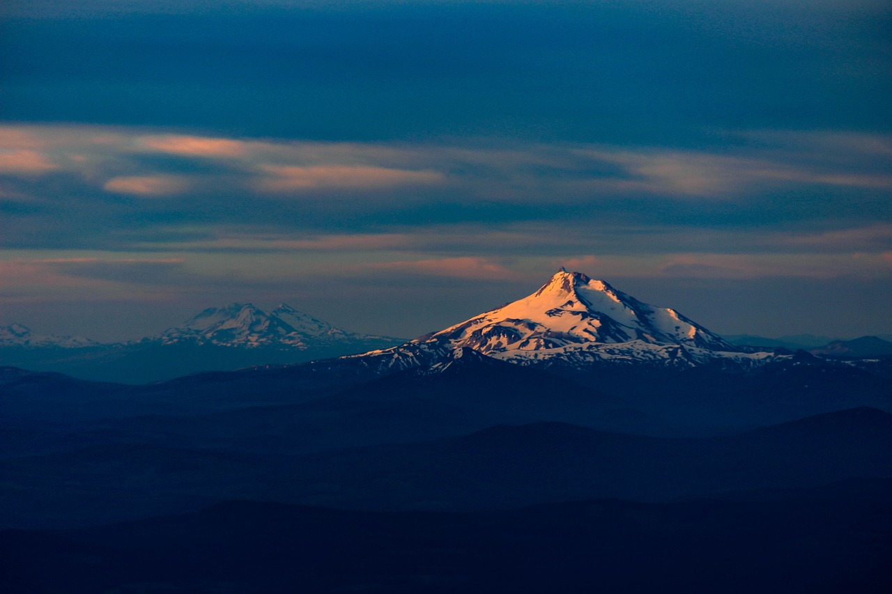 a mountain covered in snow under a cloudy sky, a tilt shift photo, by Alexander Robertson, precisionism, portland oregon, volcanoes in the background, godrays at sunset, three views