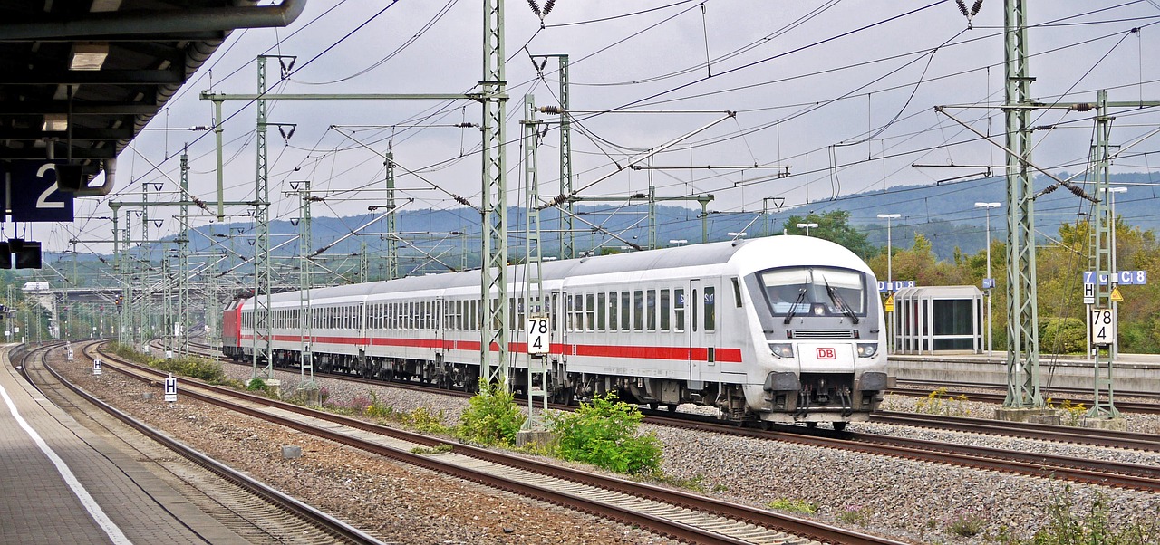 a train traveling down train tracks next to a train station, by Werner Gutzeit, flickr, silver white red details, high speed trains, darius puia, in summer