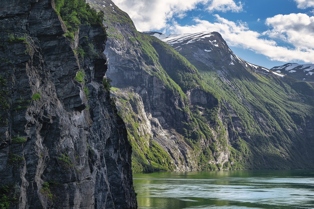 a man standing on top of a cliff next to a body of water, a detailed matte painting, by Harry Haenigsen, shutterstock, hurufiyya, norway fjord, vertical orientation, photo taken from a boat, sunlit