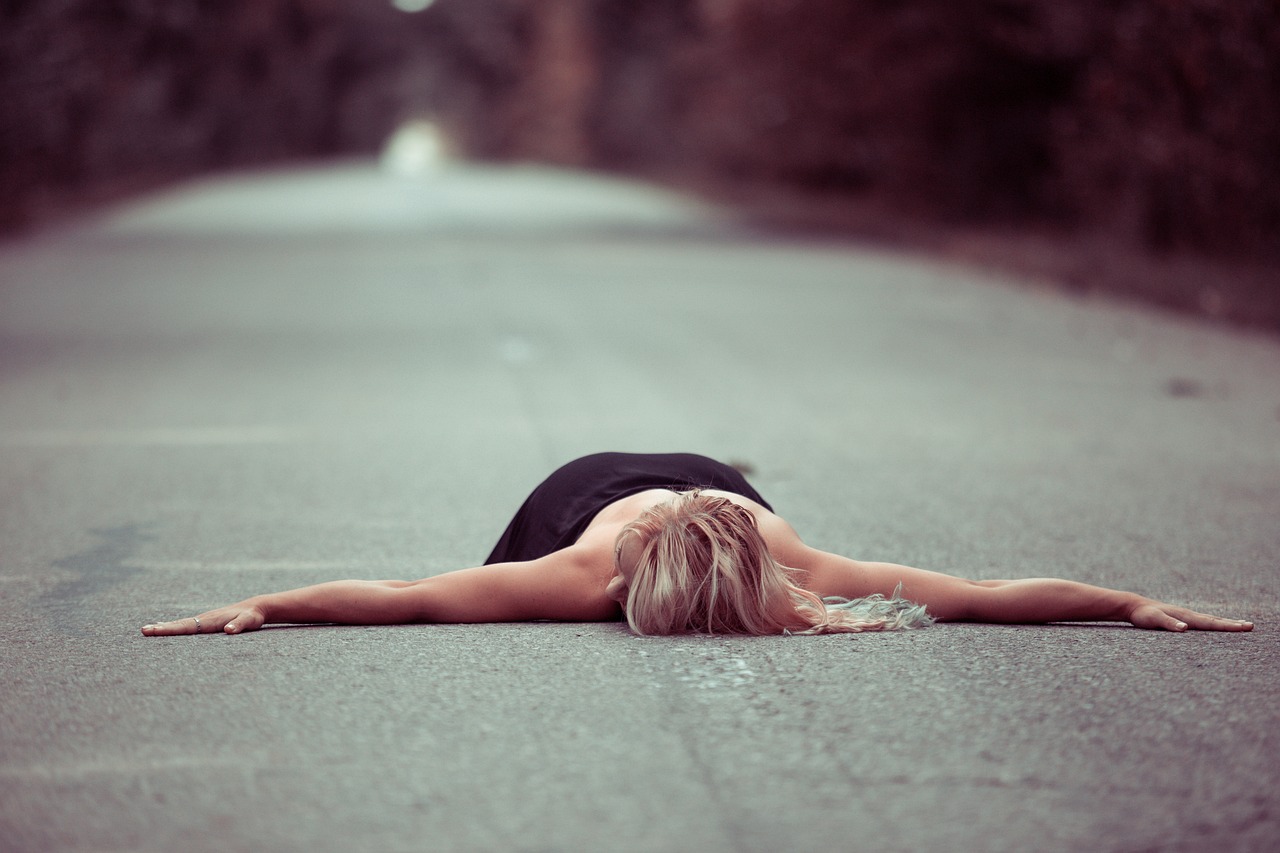 a woman laying on the ground in the middle of a road, a picture, postminimalism, blonde, arms raised, sorrow, mid body shot