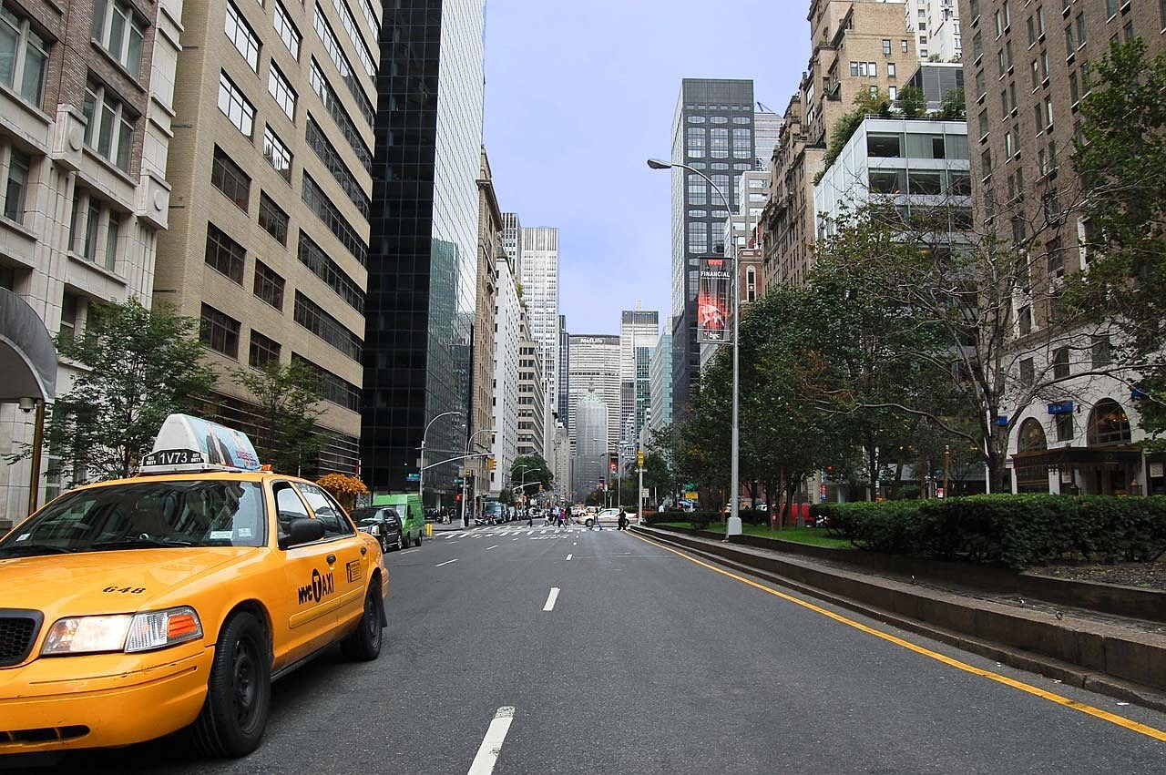 a yellow taxi cab driving down a city street, a picture, inspired by Thomas Struth, empty road in the middle, on madison avenue, avenida paulista, wikipedia