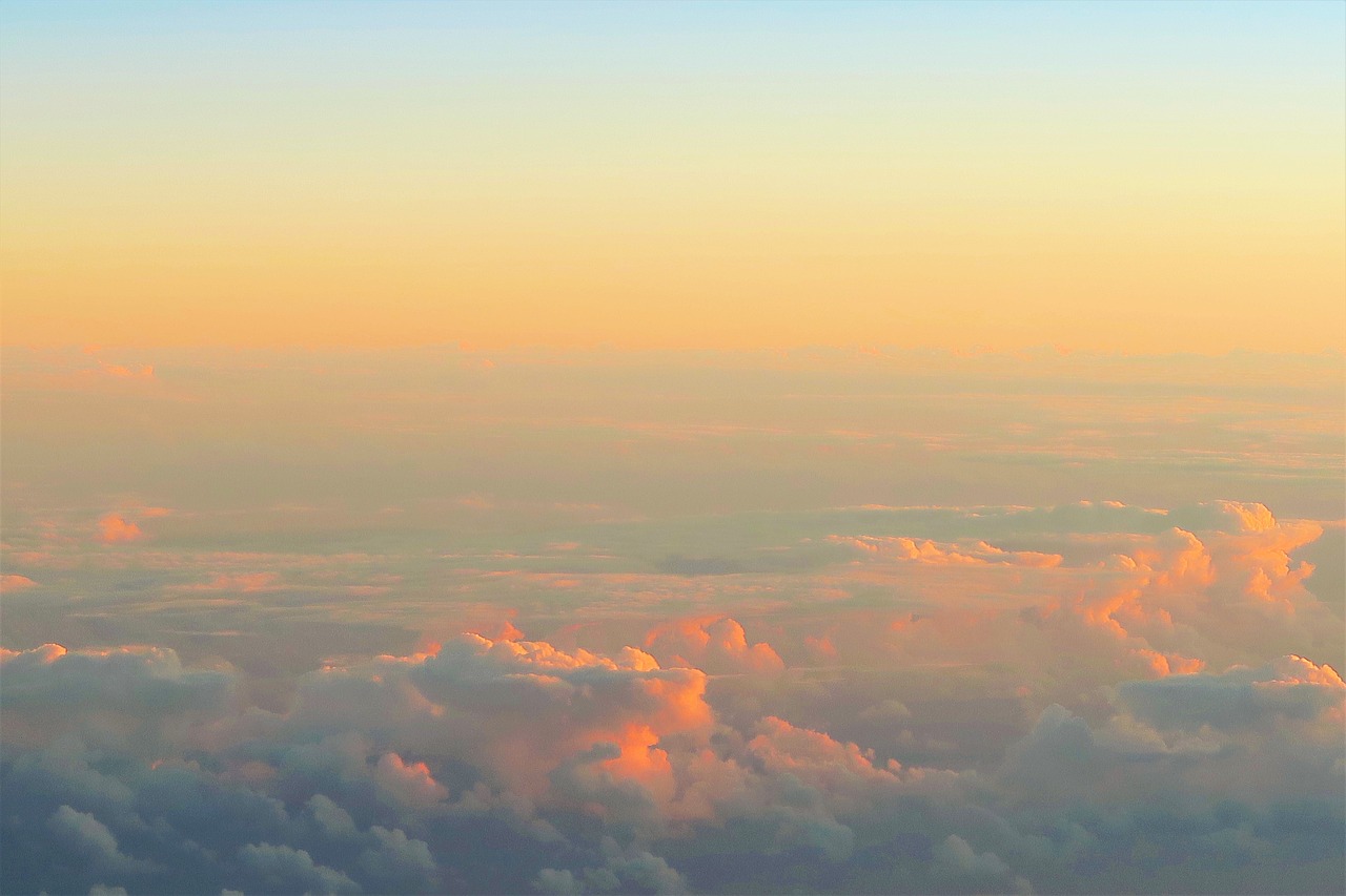 an airplane is flying high above the clouds, by Matt Cavotta, pastel orange sunset, sunset panorama, cotton candy clouds, patches of yellow sky