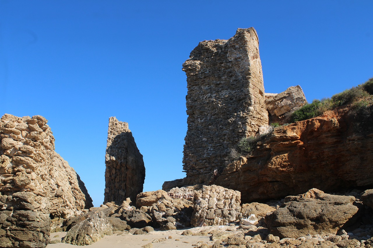 a group of rocks sitting on top of a sandy beach, romanesque, old ruins tower, rocha, year 1506, interesting details