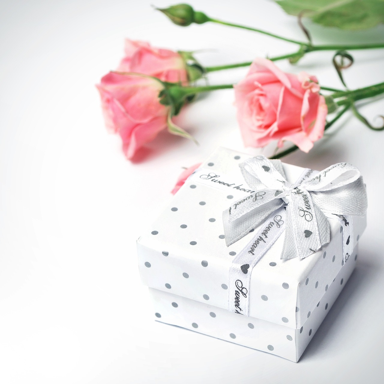 a white gift box sitting next to a pink rose, romanticism, silver jewelry, spots, high quality product image”