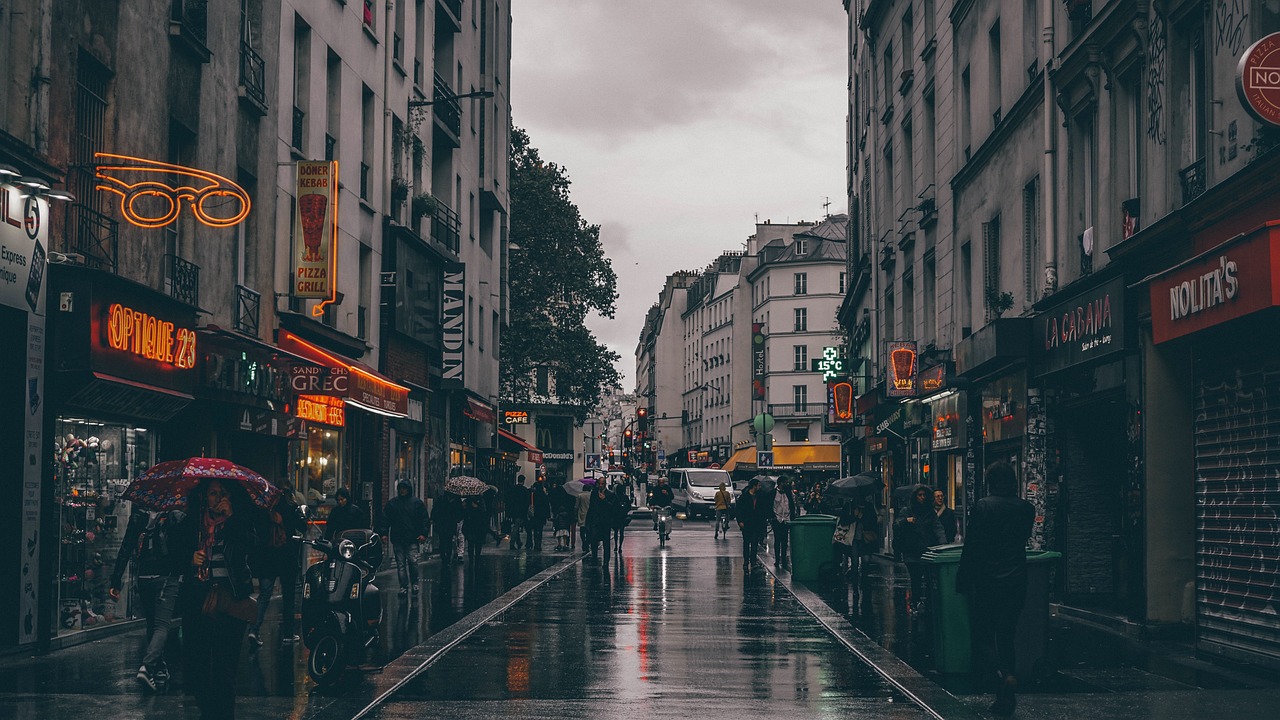 a couple of people walking down a wet street, by Raphaël Collin, unsplash contest winner, paris background, lots of shops, gloomy weather. high quality, dingy city street