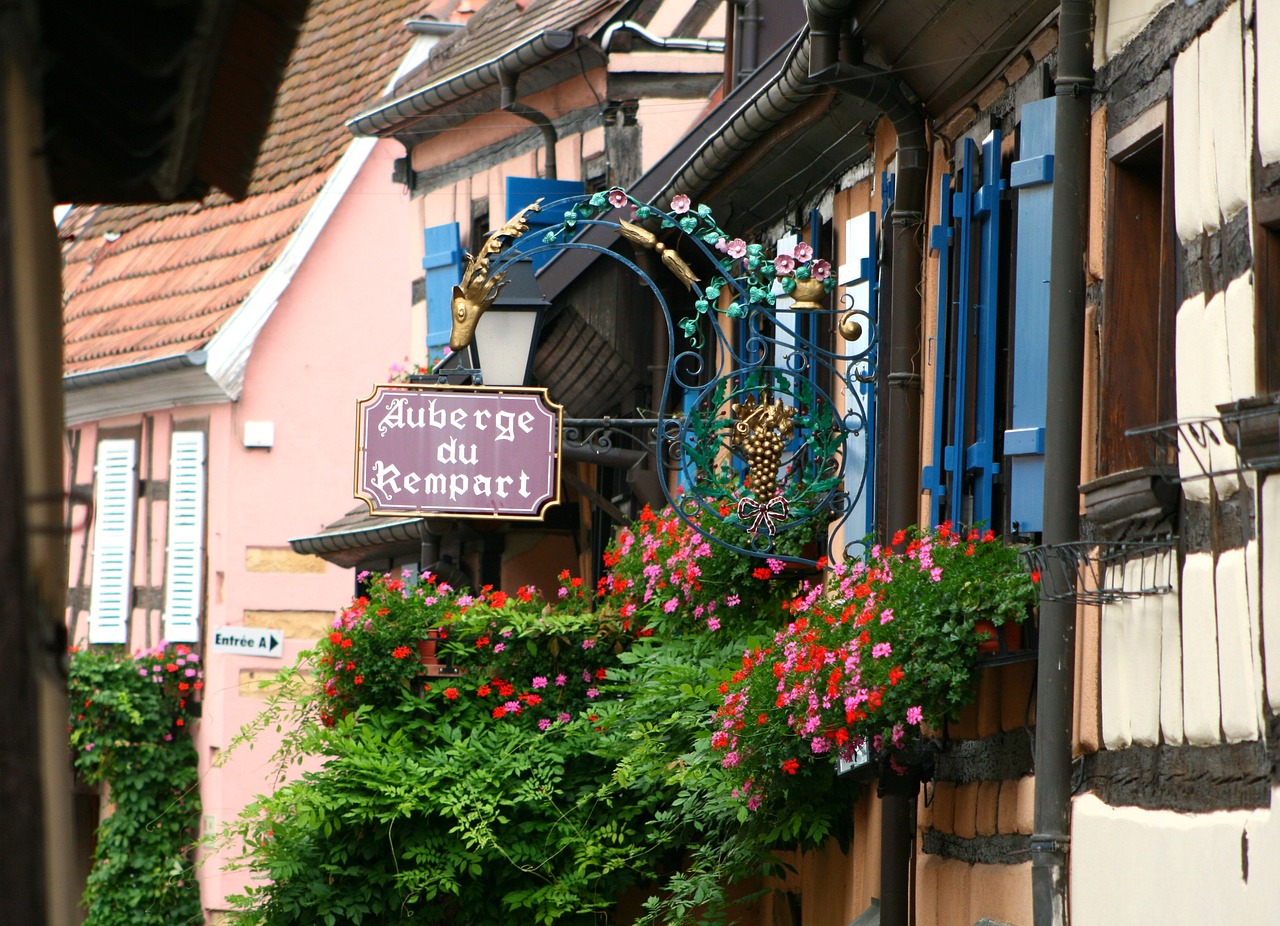 a sign hanging from the side of a building, by Juergen von Huendeberg, flickr, french village interior, wrapped in cables and flowers, rivendell, peaked wooden roofs