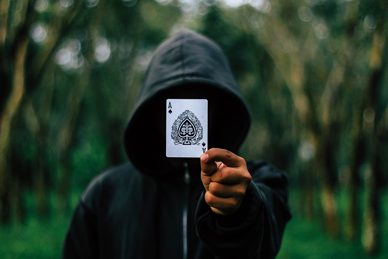 a person holding a playing card in front of their face, a picture, by Jacob Toorenvliet, unsplash, hooded cloaks, style of hydro74, an edgy teen assassin, holding it out to the camera