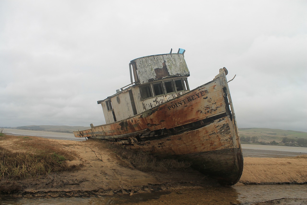 a boat sitting on top of a beach next to a body of water, a portrait, by Robert Brackman, flickr, post apocalyptic san francisco, water surrounds the ship, side view of a gaunt, musty