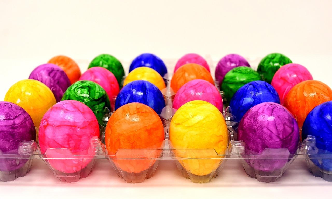 a carton filled with lots of colorful easter eggs, made of alcohol ink on parchment, with a white background, file photo, the sun is shining