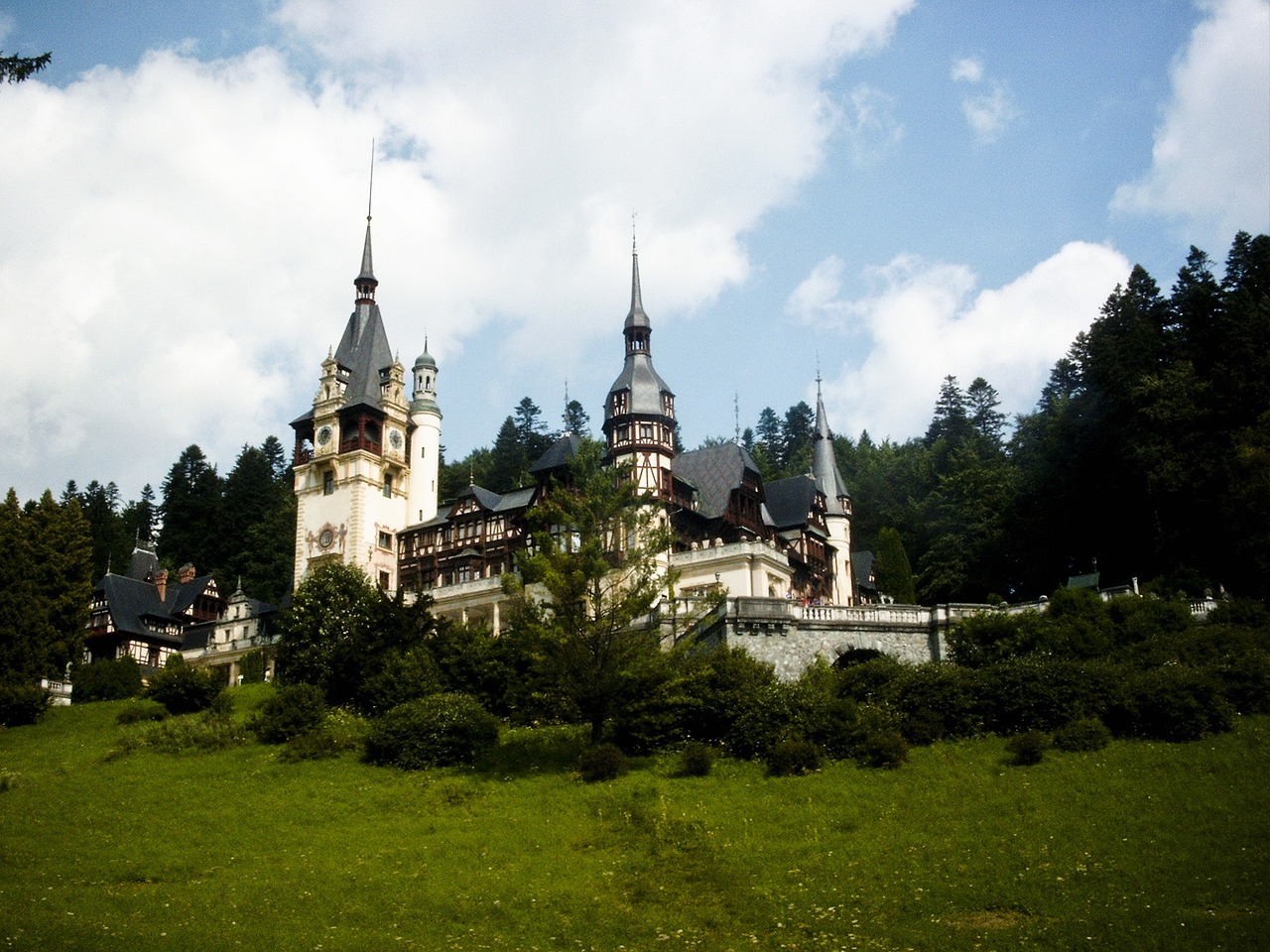 a castle sitting on top of a lush green hillside, a photo, by Eugeniusz Zak, flickr, art nouveau, black domes and spires, romanian heritage, a palace with a thousand long, a wooden