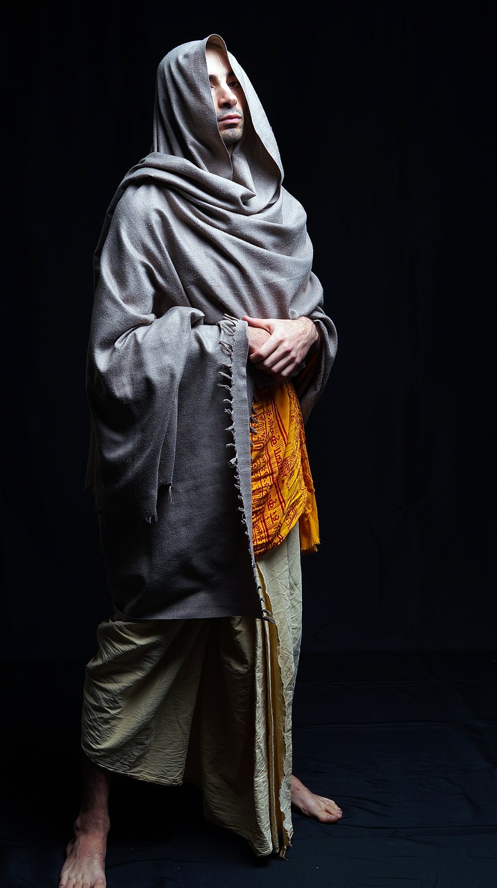 a man standing in front of a black background, inspired by Aladár Körösfői-Kriesch, hurufiyya, covered with blanket, medieval dress yellow ochre, portrait tilda swinton, young himalayan woman