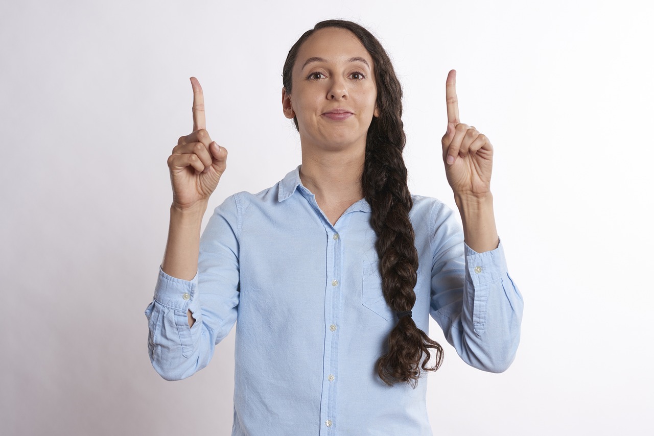 a woman holding two fingers up in the air, a stock photo, antipodeans, wearing a light blue shirt, with two arrows, funny professional photo, young middle eastern woman