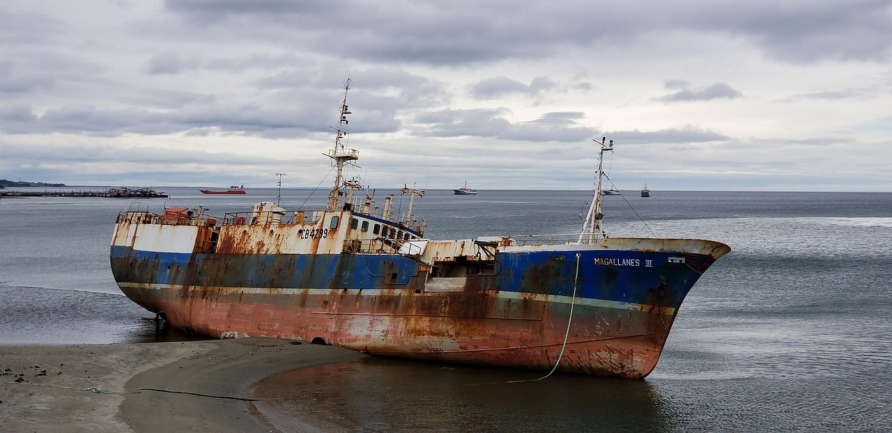 a rusty boat sitting on top of a beach next to the ocean, a portrait, by Richard Carline, pixabay, norilsk, ships in the harbor, sinking, left profile