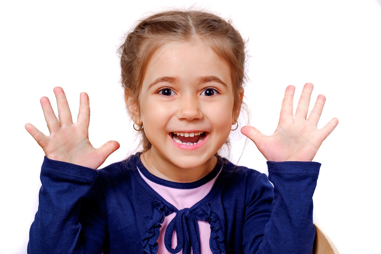a little girl sitting at a table with her hands in the air, a picture, large front teeth, istockphoto, broad shoulders, cute schoolgirl