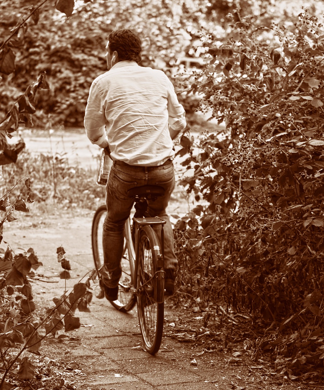 a man riding a bike down a path, inspired by August Sander, renaissance, sepia, 7 0 s photo, rear-shot, amongst foliage