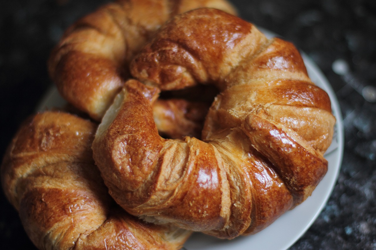 a close up of a plate of croissants on a table, by Tom Bonson, hurufiyya, shiny crisp finish, bagels, wrinkly, brown