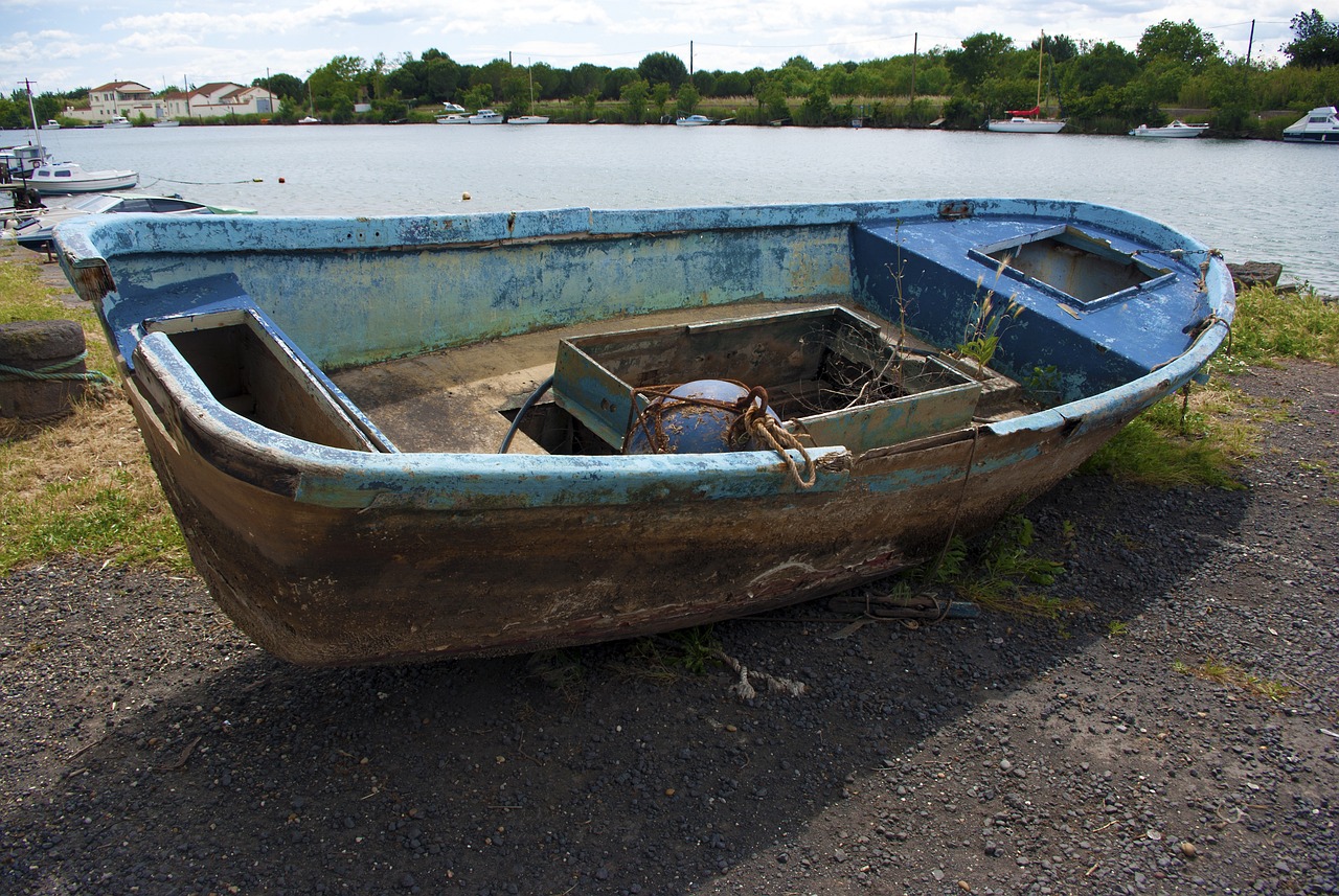 a boat sitting on top of a beach next to a body of water, shutterstock, folk art, photo of poor condition, the thames is dry, front side view, blue