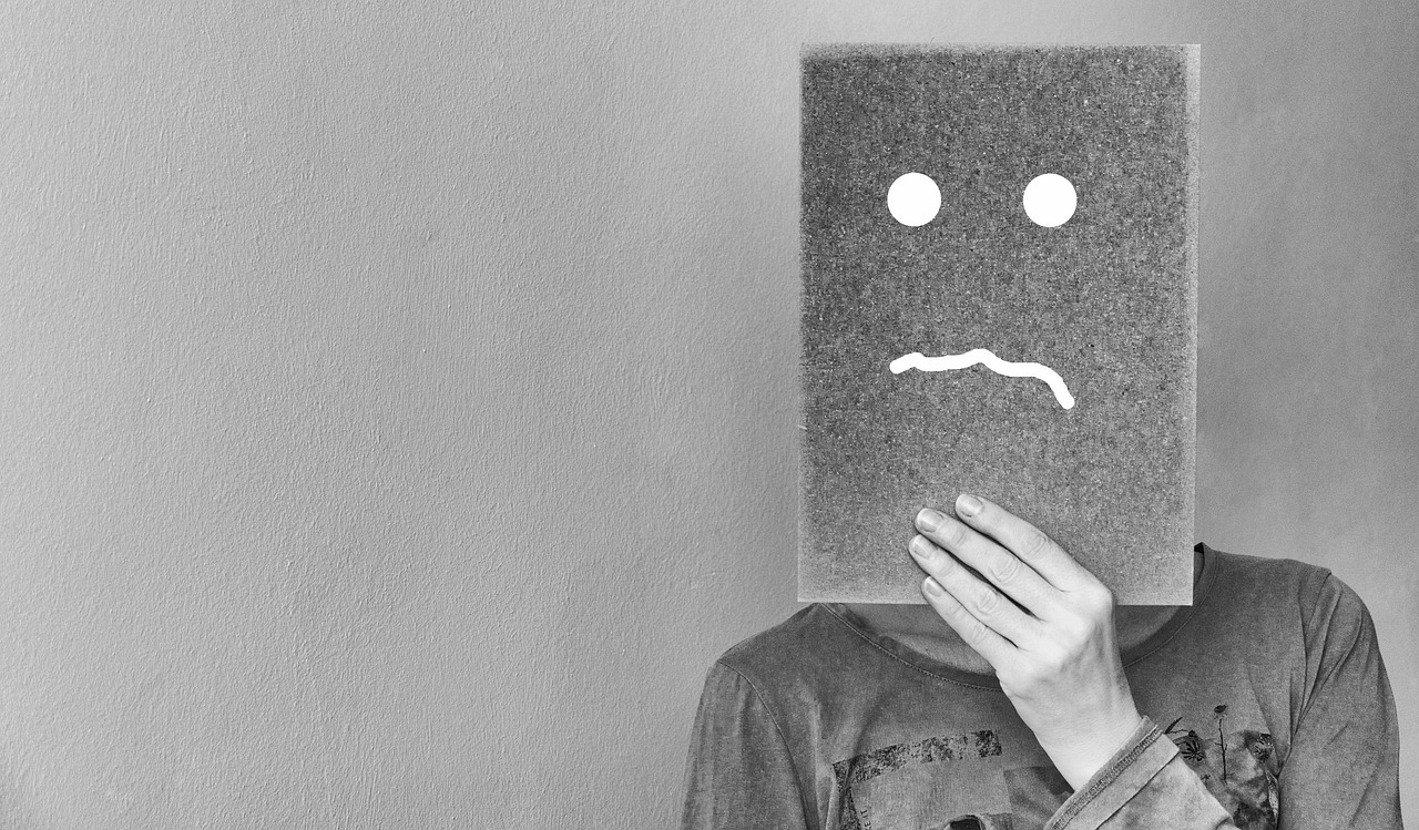 a person holding a piece of paper with a sad face drawn on it, a black and white photo, by Matija Jama, pexels, minimalism, wearing giant paper masks, desaturated!, robot face, disappointed
