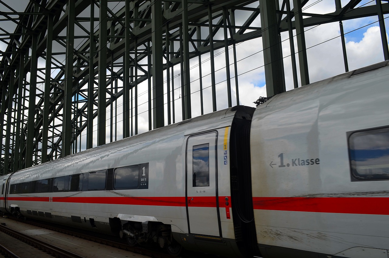 a large long train on a steel track, by Karl Völker, flickr, red trusses, next to a big window, pillar, on a cloudy day